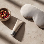 Minimalistisches Stillleben ohne Branding: UV-Schutz, Schlafsymbol und frische Zutaten als ruhige Metapher für Haut-Basics.